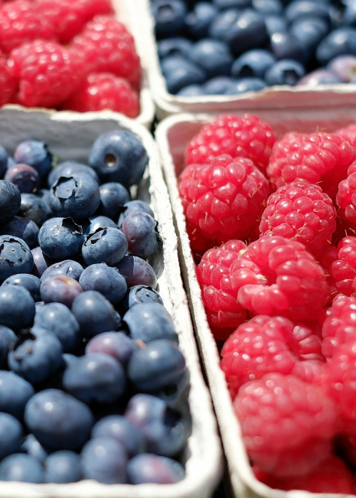 Close-up of fresh raspberries and blueberries in cartons. The vibrant red and deep blue berries are in focus, conveying a fresh, summery feel.